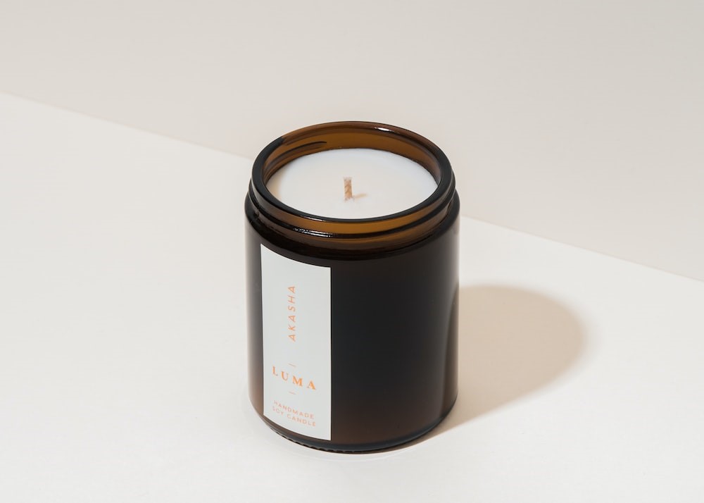 A Scented Candle in a Dark Jar, White Vertical Custom Label with Orange Font, and Minimalistic Details